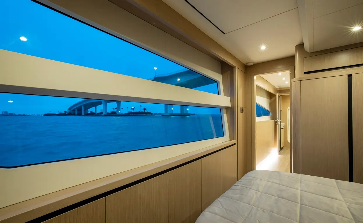 Modern interior of a yacht cabin featuring a large window showing water and a bridge, with soft lighting and minimalist design.